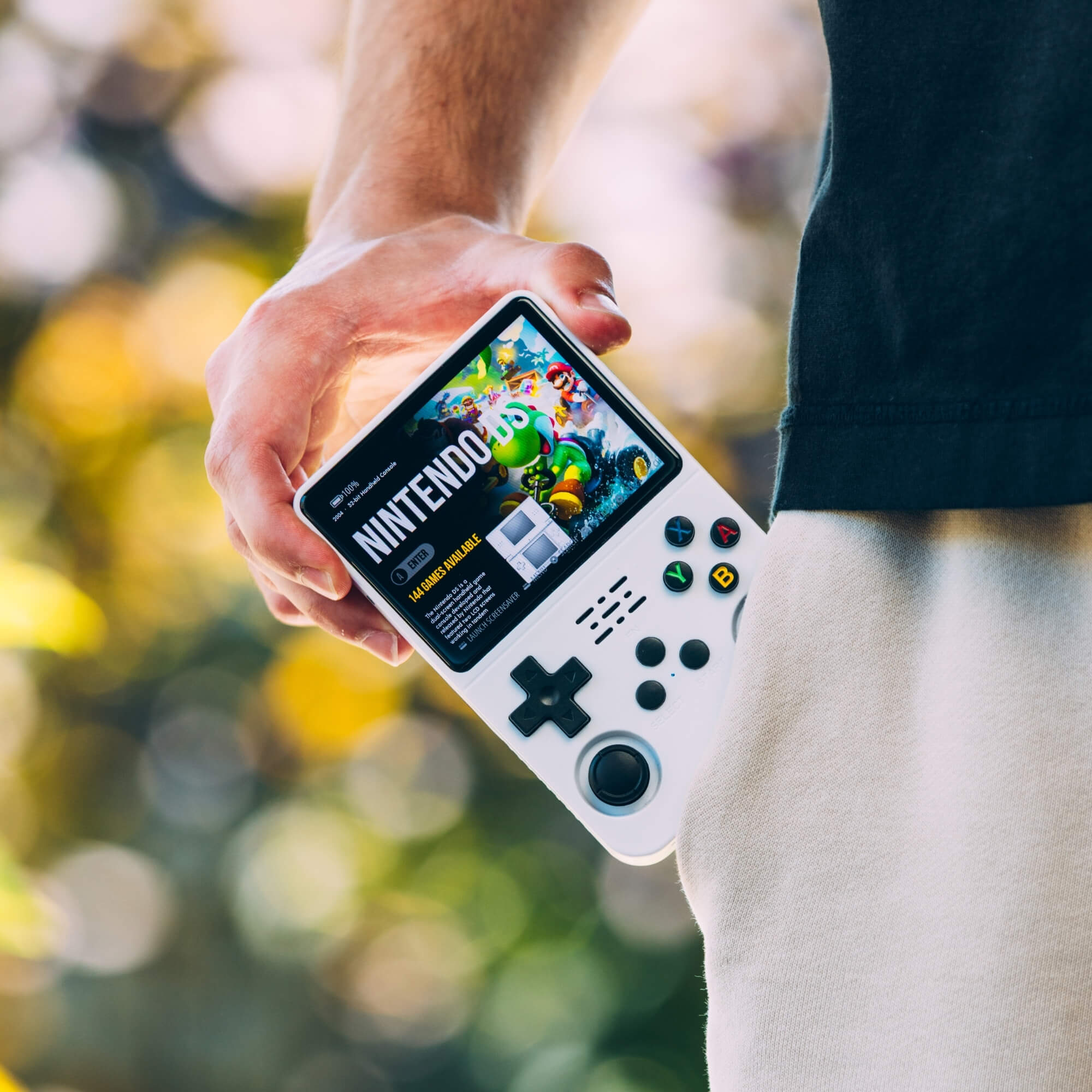Hand holding a r36s handheld gaming console with a blurred outdoor background